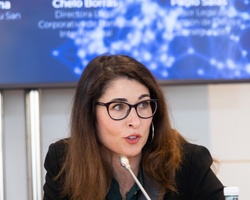 A woman is giving a presentation at a conference, addressing an audience off-camera.