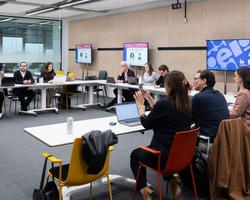 A group of professionals in a meeting room engaging in a discussion with a speaker.