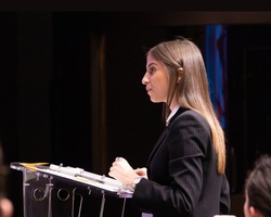 A young woman is delivering a speech at a podium in front of an audience.