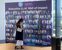 A woman is observing a wall filled with headshots representing the Executive LL.M. program.