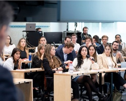 A diverse group of attentive students listening to a lecturer in a university classroom setting.