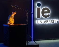 A person is presenting in front of the IE University sign.