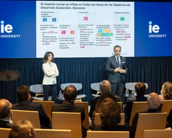 A man and a woman presenting at a conference in front of an audience, with a digital presentation about sustainable development goals displayed behind them.
