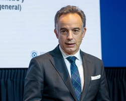 A man in a suit standing at a podium with a presentation slide behind him labeled 'Economía en general'.