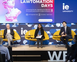 Three professionals sitting on a panel at a conference event, discussing topics in front of an audience.