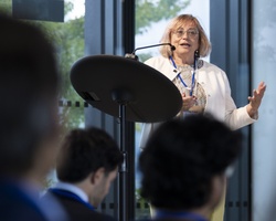 A woman is giving a speech at a podium in a conference room, addressing an audience.