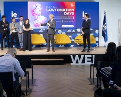 A group of people standing on a stage during an event titled 'Lawtomation Days' at a venue with audience members seated facing them.