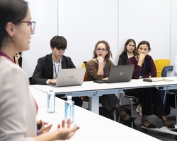 A woman is presenting to a group of attentive professionals in a corporate meeting room.
