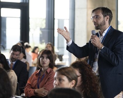 A man in a suit is speaking into a microphone in front of an audience at a conference.