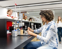 A student is conducting an experiment in a modern laboratory while others observe.