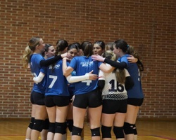 A group of young female volleyball players huddled together in a gym.