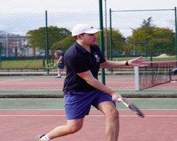 A young man is playing tennis on an outdoor court.