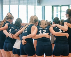 A group of young female volleyball players huddled together in a supportive formation.