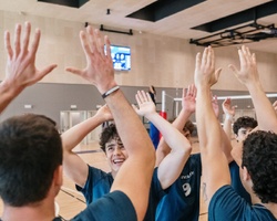 A group of young volleyball players celebrating with their hands raised.