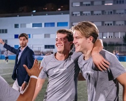 A group of young men celebrating on a sports field at night.