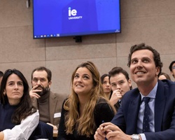 A group of people sitting in a conference room looking attentively towards a presentation screen displaying 'IE University'.