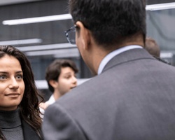 A young woman and a man in a business suit having a conversation in a busy office environment.