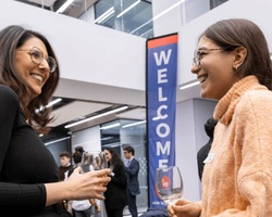 Two women smiling and talking at a welcome event in a modern office space.