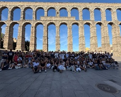 A large group of people gathered in front of a historic aqueduct under a clear blue sky.