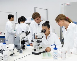 A group of students in lab coats working with a microscope in a laboratory setting.