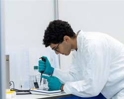 A young man in a lab coat is conducting an experiment using a pipette.
