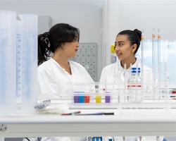 Two scientists are having a conversation in a laboratory filled with equipment.