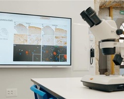 A laboratory workspace featuring a microscope and a large screen displaying scientific images.