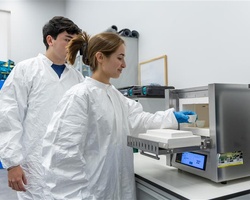Two individuals in lab coats are working with a scientific device.