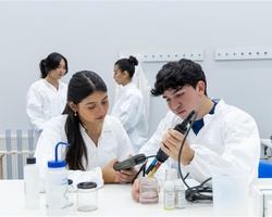 Two students in lab coats are conducting experiments with a pipette in a laboratory.