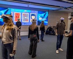 People using virtual reality headsets in a room with a large digital display.