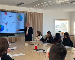 A business meeting in a modern conference room with a presenter showing charts on a screen.