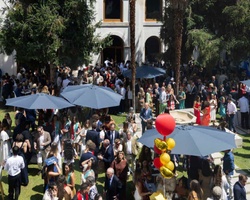 A large outdoor gathering with many people enjoying a sunny day under umbrellas.