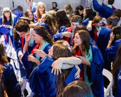 A joyful graduation ceremony with students in gowns celebrating and embracing each other.