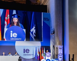 A graduation ceremony at IE University with a student speaking on stage.