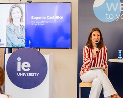A woman is speaking at an event for IE University with a presentation screen behind her.