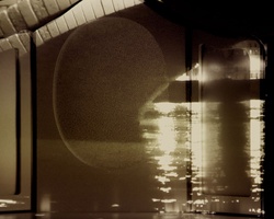 A night scene showing the illuminated reflection of a curved structure on water.