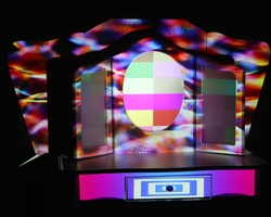 A colorful abstract projection on a three-dimensional geometric installation featuring a central circle and rectangular shapes.