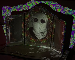 A mask displayed in a colorful, ornately shaped showcase, possibly in a dark room.