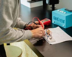 A person working on an electronic project with wires and a multimeter.