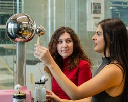 Two women are engaged in a science experiment involving a Tesla coil.