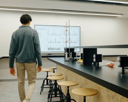 A person walking away in a modern laboratory with a large display showing graphs.