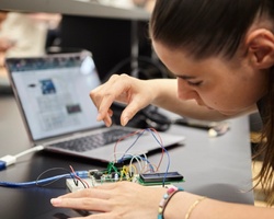 A person is focused on assembling a circuit with wires and components while working on a laptop.