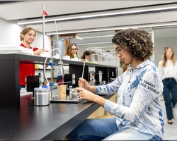 A student is conducting an experiment in a modern laboratory while others observe and participate.