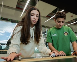 Two young people are concentrating while engaging with a tabletop activity indoors.