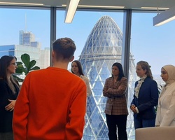 A group of professionals engaged in a discussion in a modern office with a city view.
