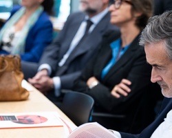 A group of professionals attending a conference, with a focus on a man reading a document.