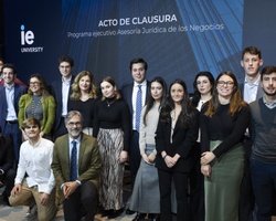 A group of people, possibly students and professors, standing together at a closing ceremony in front of a backdrop that reads 'IE University'.