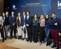 A group of individuals standing together in a formal event at IE University, with a banner reading 'ACTO DE CLAUSURA' in the background.