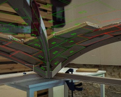 A close-up view of a woodworking project featuring curved wooden pieces being held in place with visible measurement markings.
