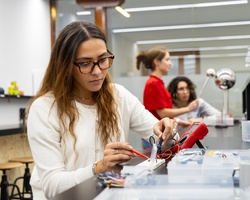 A woman is working on electronics with a multimeter in a modern lab environment.